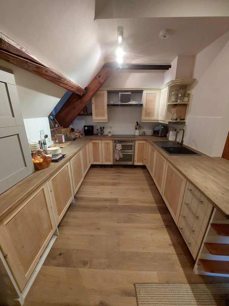 A modern kitchen featuring wooden cabinets, a sleek countertop, and exposed wooden beams. The space includes a stove, sink, and various kitchen appliances, with a warm and inviting atmosphere.