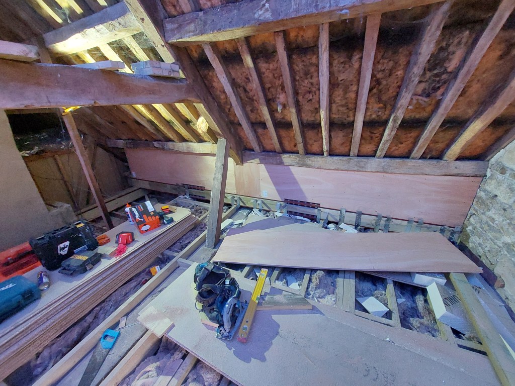 A view of an attic under construction, featuring exposed wooden beams, insulation, and construction tools scattered across the floor.