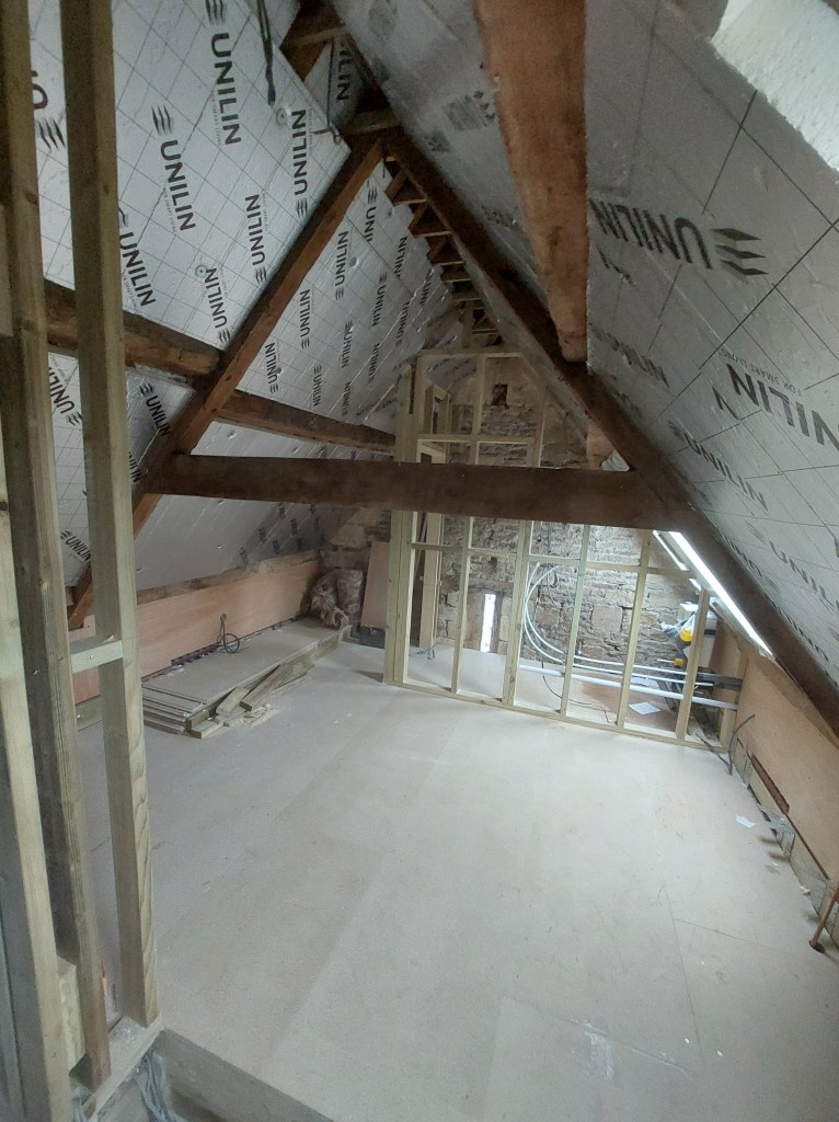 An unfinished attic space featuring wooden beams, insulation material, and construction framing.