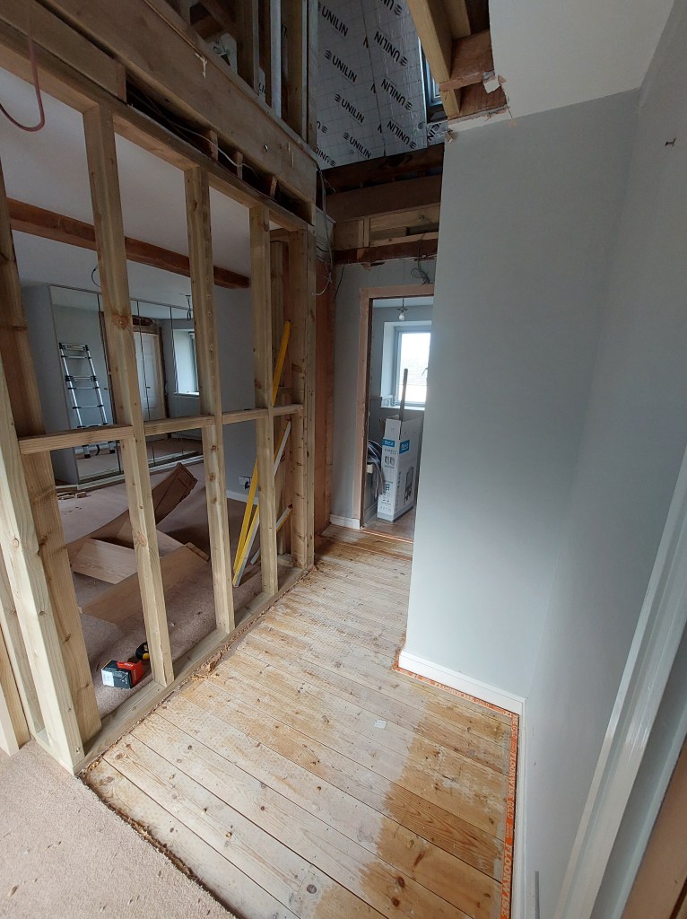 Interior view of an unfinished hallway with exposed wooden framing and a partially removed floor covering.