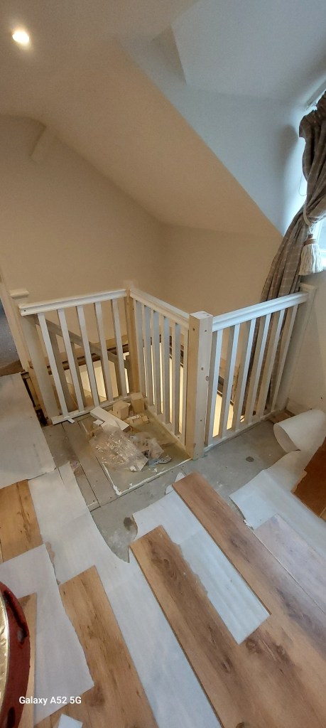 View of a staircase landing with a wooden railing and partially laid floor planks.