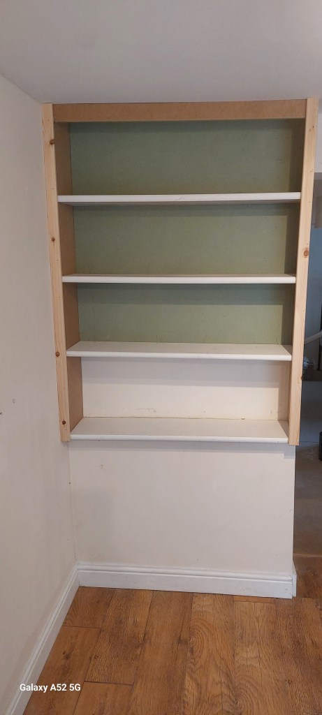 A wooden bookshelf with three white shelves against a green wall.