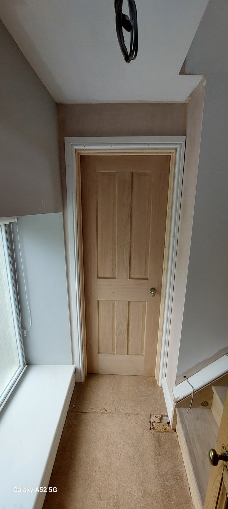 View of a hallway with a wooden door, light fixture hanging from the ceiling, and a partial view of a staircase.