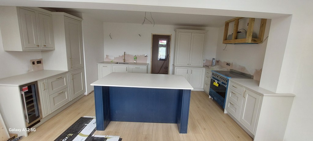 Modern kitchen interior featuring white cabinets, a central island with a blue base, and a blue oven. Natural wood flooring and minimalistic design elements are present.