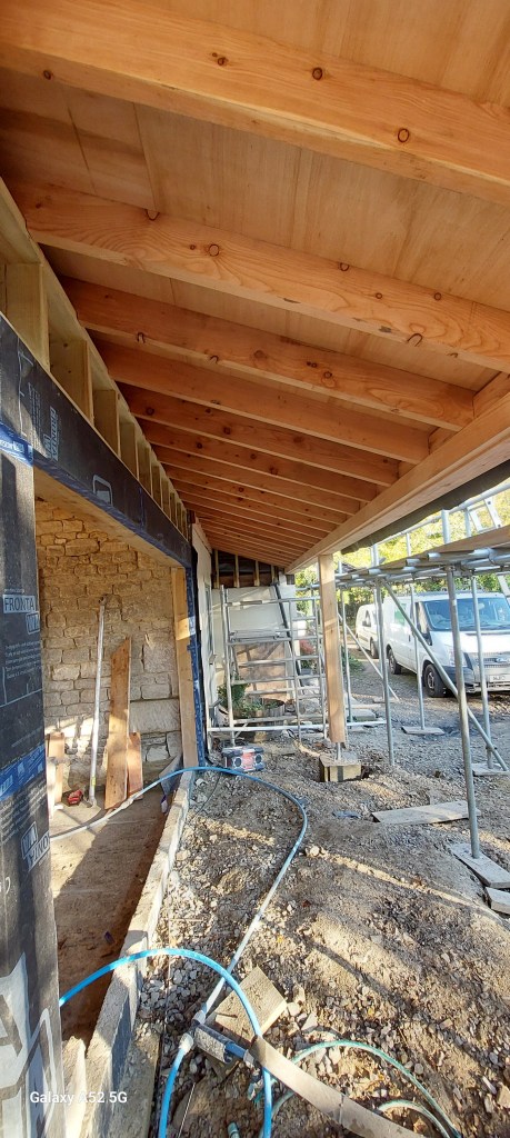 Interior view of a construction project showing wooden beams and scaffolding, with tools and a van visible in the background.