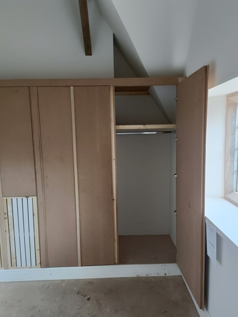 Interior view of a partially constructed closet with wooden framework, light walls, and a window.