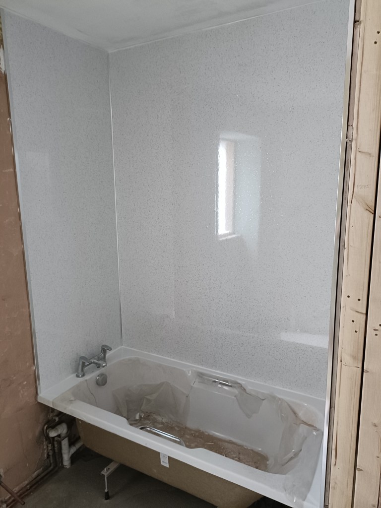 A newly installed bathtub with protective covering, surrounded by light-colored walls and partially exposed wood framing.