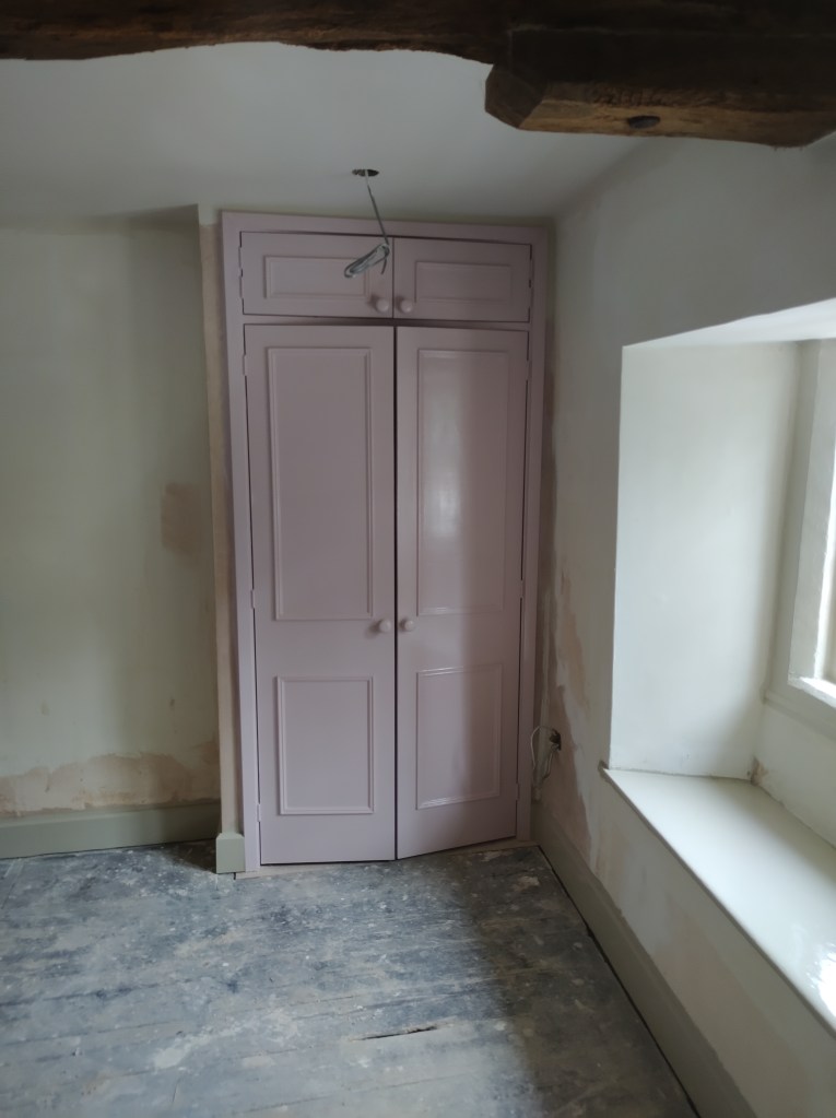 Interior view of a room featuring a pale pink closet with two doors, a small window with a ledge, and a partially painted wall.