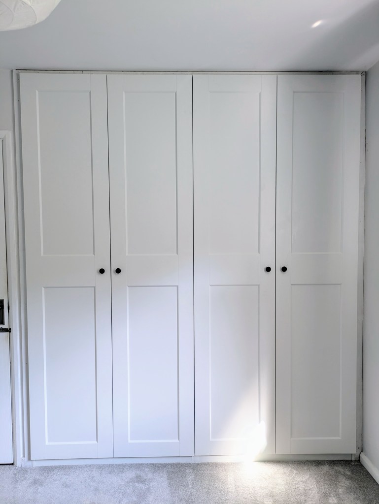 A modern white wardrobe with flat panel doors and black knobs in a bright room.